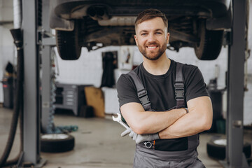 Smiling bearded mechanic while standing with crossed arms and holding wrenches in a car service