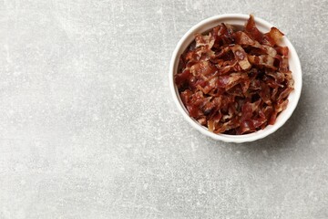 Pieces of tasty fried bacon in bowl on gray table, top view. Space for text