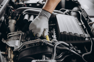 Close-up shot of unrecognisable man wearing gray glove inspecting car engine and interior of hood of car