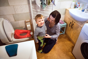 Mom is helping toddler boy use the toilet. Potty-trained little boy in the bathroom.