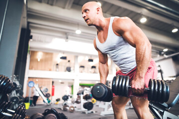 Close up of man performing single arm dumbbell row in bent-over position. Routine workout for physical and mental health.