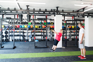 Overweight woman exercising in gym. Personal trainer couching her and helping her.