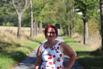 A woman in a red dress and glasses is walking down a path in a forest