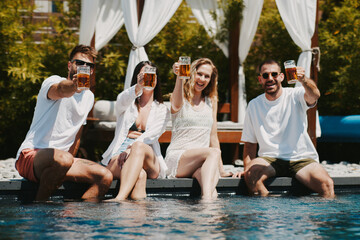 Young group of people having fun by the pool and doing toast with beer