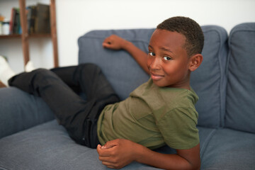 Cute carefree african american boy kid lying on sofa in olive t-shirt and black pants, having rest after returning home from school, enjoying free leisure time and childhood doing nothing