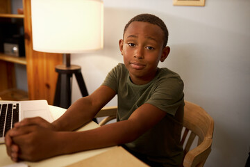 Tired sad bored smart intelligent black boy kid sitting at table in front of laptop, feeling...