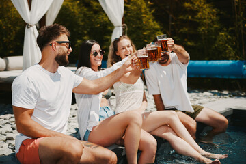 Young group of people having fun by the pool and doing toast with beer