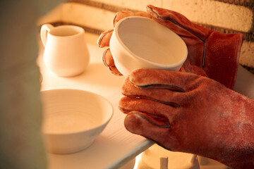 Woman professional potter in gloves holding taking ceramic bowl from kiln