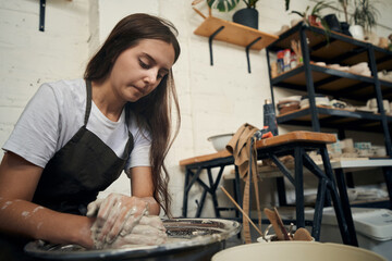 Woman potter working with pottery wheel making future clay product