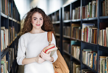 Young female student in library, looking for books, preparing for final exam.