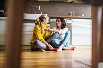Mother and mature daughter in kitchen, sitting on floor and talking. Closeness of mom and her adult...