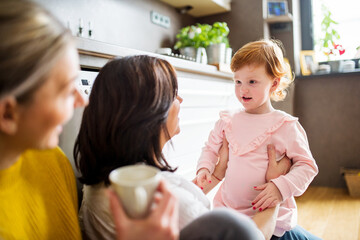 Mother, grandmother and little granddaughter in kitchen, sitting on floor. Family time, three...