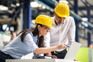 Two project managers standing in modern industrial factory. Manufacturing facility with robotics,...