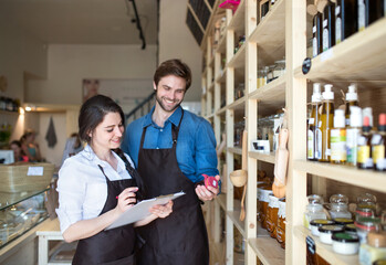 Two shop assistants in package-free store using reusable containers, checking inventory. Zero waste...