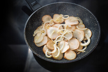 Jerusalem artichoke or topinambur (Helianthus tuberosus) roasted with onions in a frying pan, healthy root vegetable, rich in inulin for slimming and diabetes diet, copy space
