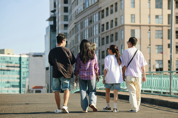 Four friends casually walking in the city, captured from behind with buildings in the background