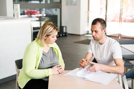 Overweight woman consulting with trainer, discussing fitness goals. Customizing exercise program with gym coach.