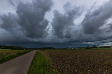 Landschaftsaufnahme von einer Gewitterwolkenformation, über Felder und Wiesen.