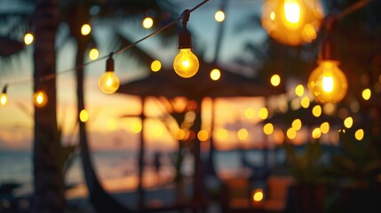 Fototapeta premium Blurred bokeh light on sunset with yellow string lights decor in beach restaurant. Outdoor string lights hanging on a line in backyard