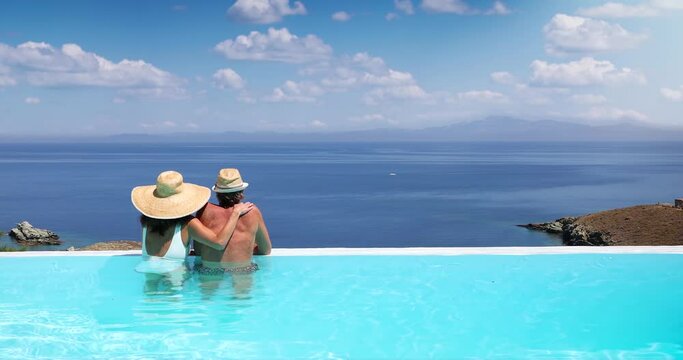 A couple hugging at the edge of an infinity pool and enjoying the view to the blue, mediterranean sea during summer vacation time