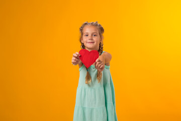 Child girl holding red paper heart over yellow background. Love, care and Valentine day concept