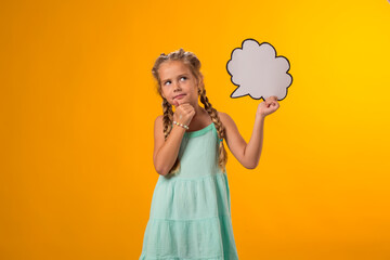 Thoughtful kid girl holding cloud bubble card over yellow background. Dreaming concept