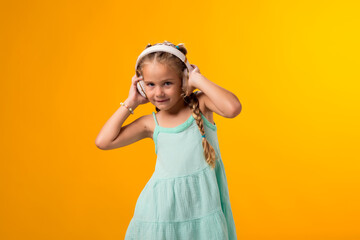 Smiling kid girl enjoying music in headphones on yellow background. Lifestyle and leasure concept