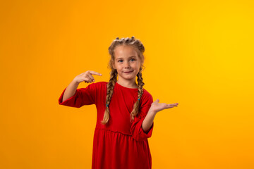Smiling child girl pointing to an empty place on yellow background. Advertisement concept