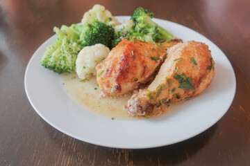 Two chicken legs with a side dish of broccoli and cauliflower on a white plate