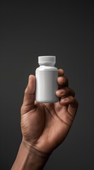 A close-up of a hand holding a blank white pill bottle against a dark background, suitable for medical and pharmacy concepts.