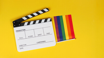 Clapper board and rainbow pride flag on yellow background.