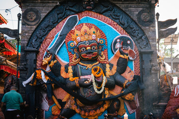 Elaborate deity statue decorated with flowers and vibrant colors in a Kathmandu, Nepal temple. The detailed sculpture stands in a brightly painted niche, exuding a sacred and cultural atmosphere.