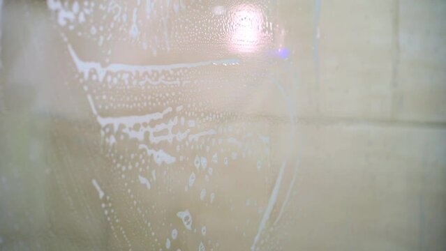 a man washes glass with a sponge and detergent.
Foam flows down the glass