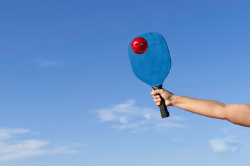 Arm hitting red pickleball ball with blue pickleball scoop