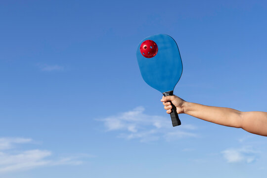 Arm hitting red pickleball ball with blue pickleball scoop