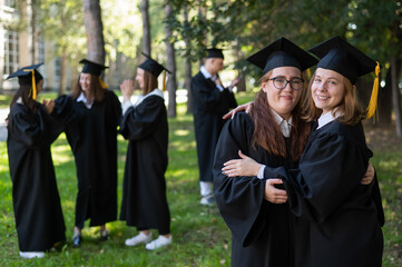 Group of happy students in graduation gowns outdoors. In the foreground, two young girls...