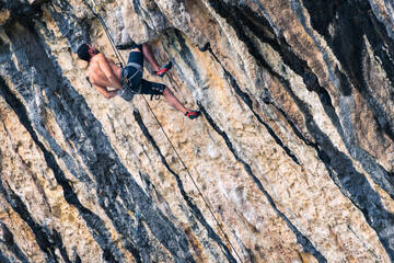 A man climbs a wall. He has his hands loose and holds himself by just jamming his knee into the wall