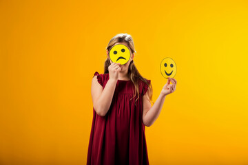 Kid girl holding sad emoticons in front of her face. Mental health, psychology and children's emotions concept