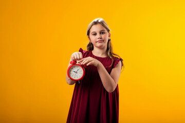 Smiling kid girl holding an alarm clock in hand and pointing finger at it. The concept of...