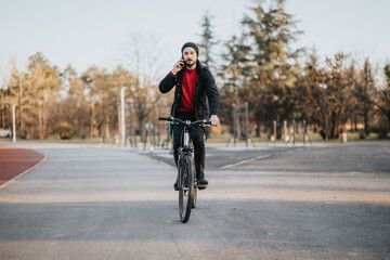 A stylish adult male enjoys a relaxing bike ride in a serene park setting, multitasking by chatting...
