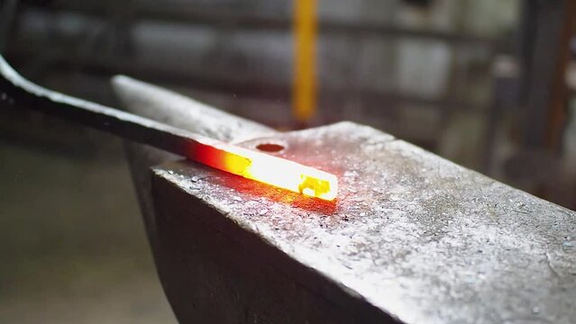 Blacksmith forging a iron bar on anvil block. A red-hot part and a sledgehammer close-up. The blows of the sledgehammer send sparks flying in different directions. Slow motion FHD footage.
