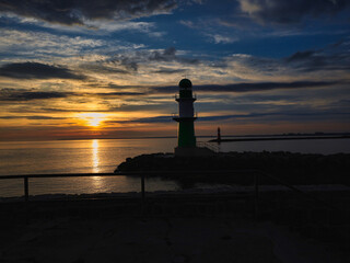 Fototapeta premium Sonnenaufgang über der Ostsee mit Blick auf das grün-weiße Molenfeuer an der Hafeneinfahrt, maritime Morgenstimmung an der Mole, Warnemünde, Rostock, Mecklenburg-Vorpommern, Deutschland
