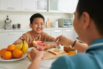 Smiling boy waiting for father making sandwiches for breakfast