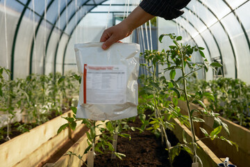 Organic farming. Male hand with package of biological fungicide on background of polycarbonate...