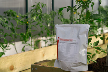 Organic farming. A fragment of a greenhouse with tomatoes with a package of biological fungicide - Trichoderma in the foreground close-up.