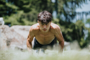 Young athletic man performing push-ups on the grass in an outdoor setting, highlighting fitness, strength, and commitment to calisthenics.