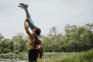A muscular man lifting his female partner outside, showcasing strength, flexibility, and balance...