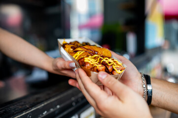 Close-up of hands exchanging a hot dog with toppings, vibrant street food concept