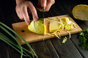 Preparing a vitamin salad of cabbage and green onions on the kitchen table by the hands of a chef.