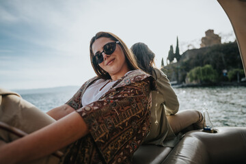 A joyful young woman with sunglasses smiles while sitting on a boat, with calm waters and nature in...